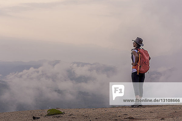 Side view of female hiker with backpack standing on mountain during foggy weather