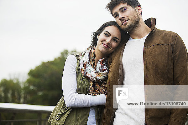 Woman resting on boyfriend's shoulder while walking against clear sky