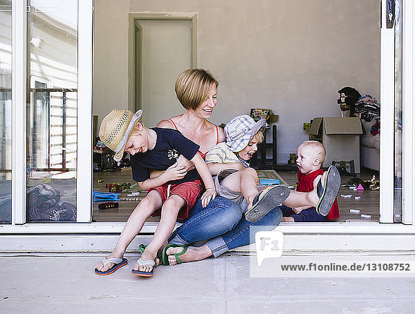 Mutter spielt mit Kindern  während sie zu Hause auf der Türschwelle sitzt
