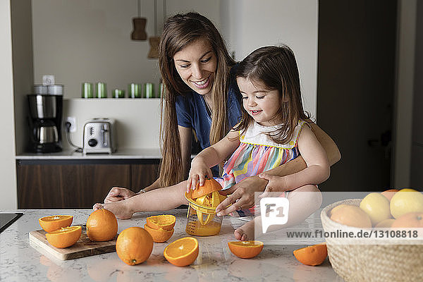 Mutter sieht Tochter an  die Orangen drückt  während sie auf einer Kücheninsel sitzt