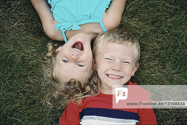Overhead view of siblings lying on grassy field in yard