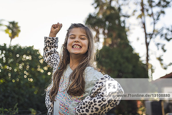 Niedrigwinkel-Porträt eines glücklichen Mädchens  das gestikulierend im Hof gegen den Himmel steht
