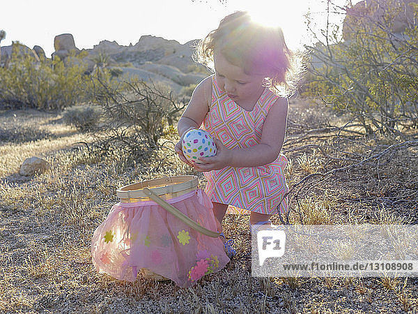 Kleines Mädchen hält buntes Osterei  während es auf Grasfeld gegen den Himmel steht