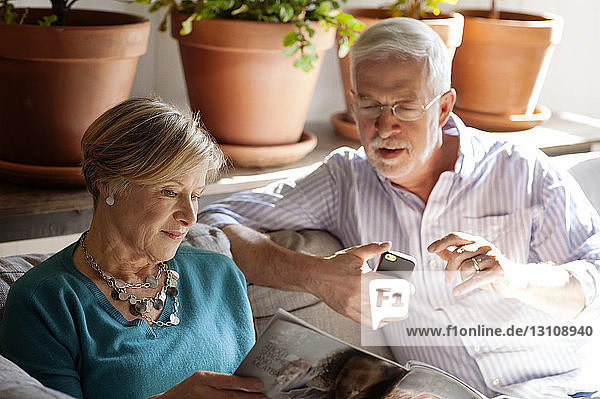 Senior couple looking at magazine while sitting on sofa