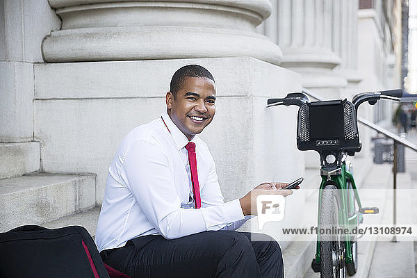 Portrait of smiling businessman using mobile phone while sitting on steps