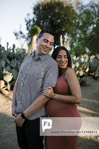 Happy couple standing against plants in park during sunset
