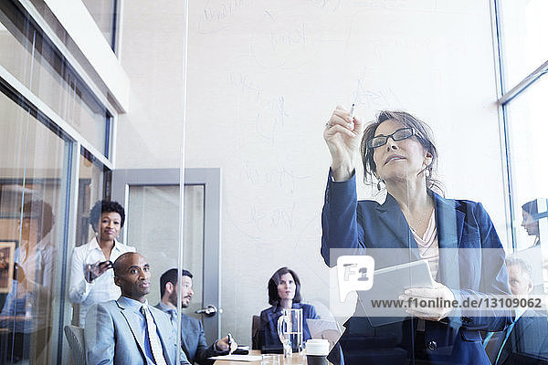 Businesswoman writing on glass wall in meeting