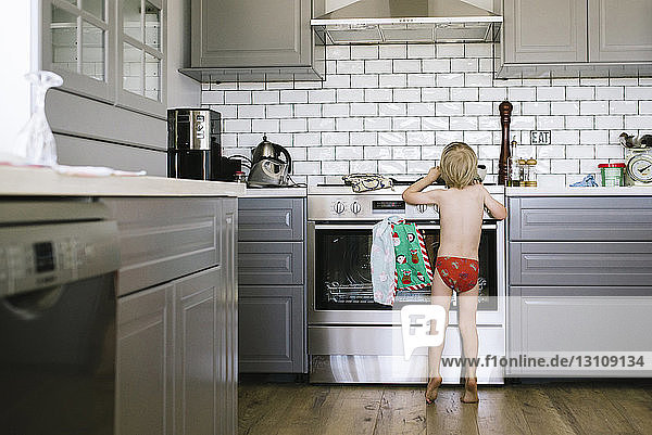 Rückansicht eines Jungen ohne Hemd  der nach etwas greift  während er in der Küche steht