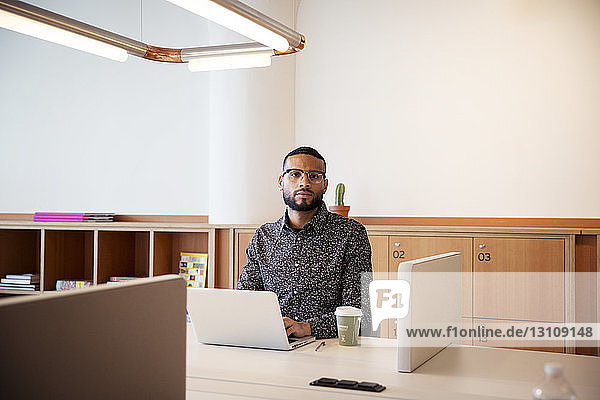 Porträt eines Geschäftsmannes mit Laptop-Computer am Tisch im Büro
