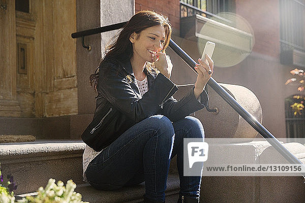 Glückliche Frau  die ein Smartphone benutzt  während sie auf einer Treppe sitzt