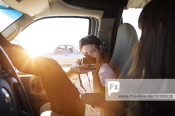 Man photographing woman through instant camera while sitting in camper van
