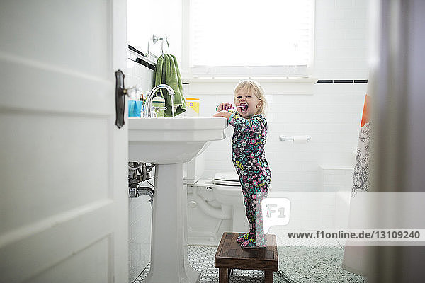 Porträt eines Mädchens beim Zähneputzen auf einem Hocker im Badezimmer