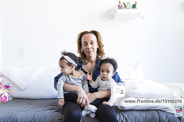 Portrait of mother holding daughters while sitting on bed