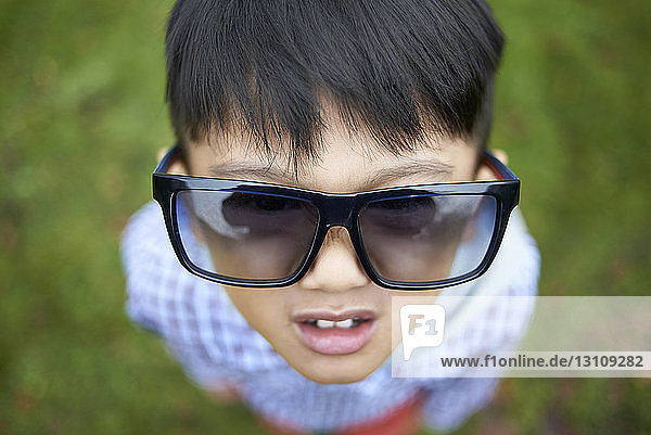 Weitwinkelaufnahme eines Jungen mit einer übergroßen schwarzen Sonnenbrille  der auf dem Spielfeld im Park steht