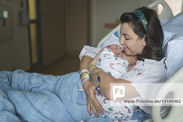 Mother kissing newborn son while relaxing on bed at hospital