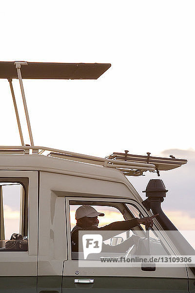 Seitenansicht eines Mannes  der beim Fahren eines Fahrzeugs im Serengeti-Nationalpark gegen den Himmel zeigt