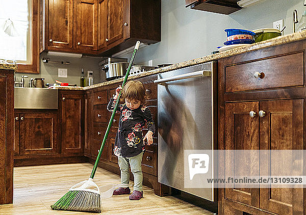Mädchen putzt zu Hause die Küche mit einem Mopp