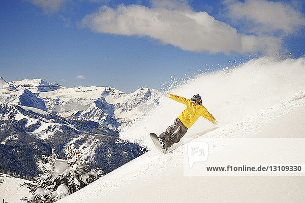 Mann beim Snowboarden auf schneebedecktem Berg gegen den Himmel