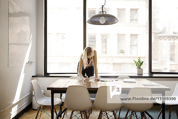 Businesswoman writing at desk in board room at creative office