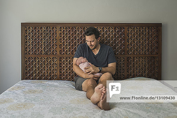Father carrying newborn daughter while sitting on bed
