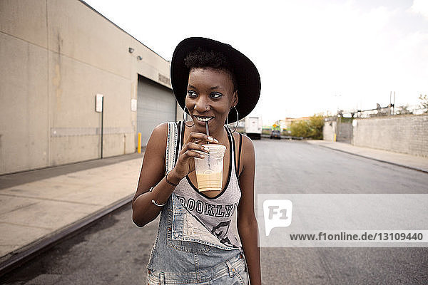 Happy woman looking away while drinking juice on street