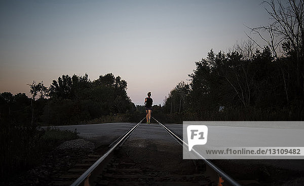 Rückansicht einer Frau  die in der Dämmerung auf einem Bahngleis gegen klaren Himmel joggt