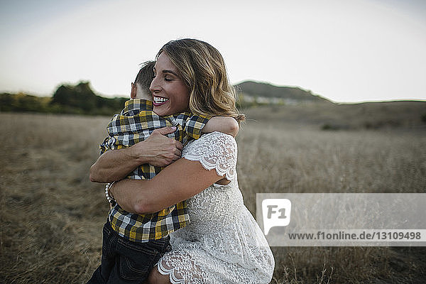 Cheerful mother embracing son while crouching on field