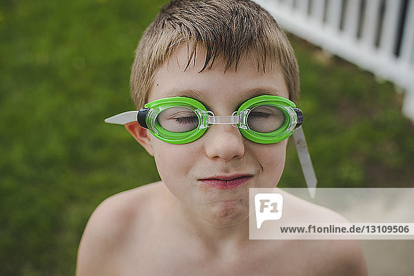 Weitwinkelaufnahme eines Jungen ohne Hemd mit Schwimmbrille  der im Hof steht