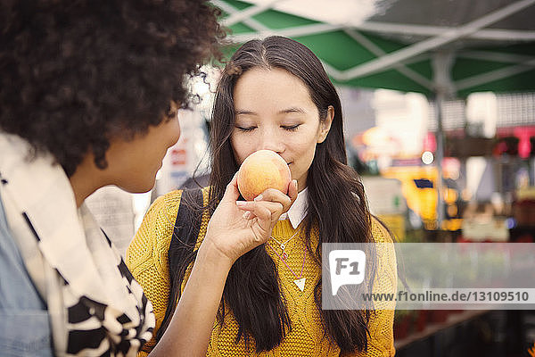 Woman smelling fruit held by friend at market