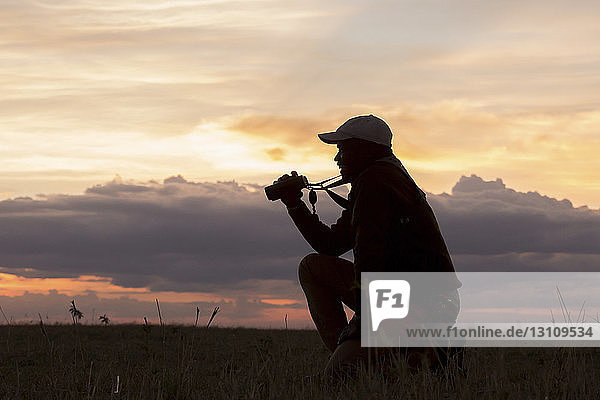 Seitenansicht eines Mannes  der bei Sonnenuntergang auf einem Feld im Serengeti-Nationalpark kniet