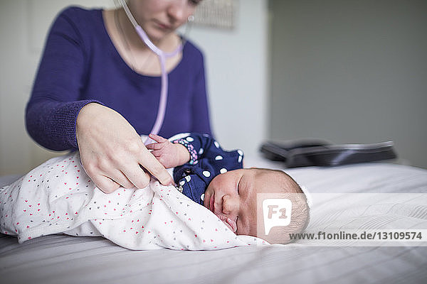 Hebamme untersucht neugeborenes schlafendes Mädchen mit Stethoskop am Bett zu Hause