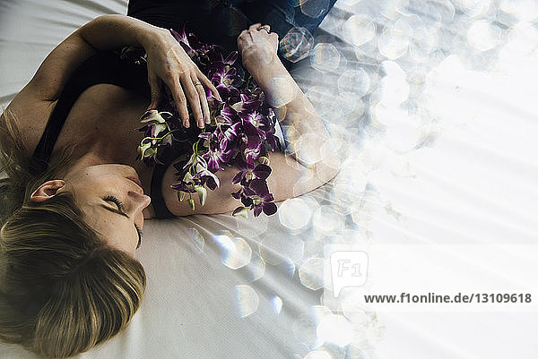 Hochwinkelaufnahme einer verführerischen Frau mit Blumen  die zu Hause auf dem Bett liegt