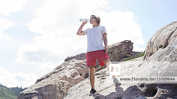 Niedrigwinkelansicht eines Menschen  der Wasser trinkt  während er auf einem Felsen vor klarem Himmel steht