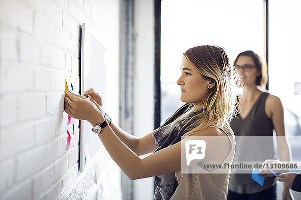Geschäftsfrau klebt Zettel an die Wand im Kreativbüro