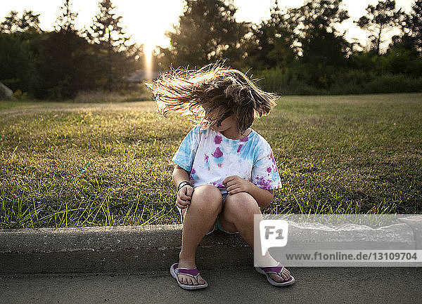 Verspieltes Mädchen  das bei Sonnenuntergang im Park sitzt und mit den Haaren wackelt