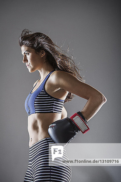 Frau mit Boxhandschuhen schaut weg  während sie vor grauem Hintergrund steht