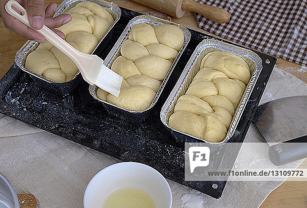 Gekrümmte Bäckerhand  die Eiweiß mit einem Pinsel auf das Brot im Behälter aufträgt