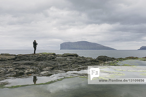 Hiker standing on rocks against sea and cloudy sky