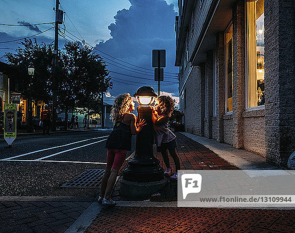Sisters looking at lamp post while standing at sidewalk in city