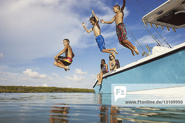 Niedrigwinkelansicht von glücklichen Jungen  die vom Boot auf See gegen den Himmel springen