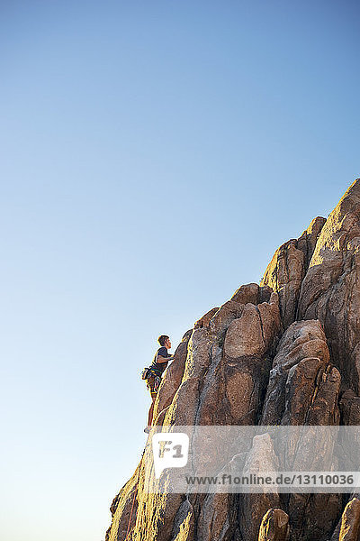 Tiefblick auf einen Mann  der am Fels klettert  bei klarem blauen Himmel