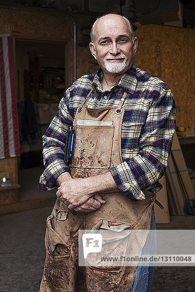 Zuversichtlicher Senior-Handwerker steht vor der Werkstatt