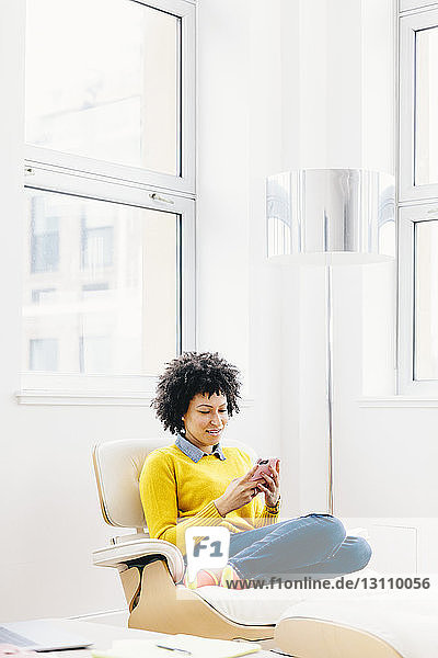 Geschäftsfrau benutzt Smartphone  während sie im Büro auf einem Stuhl sitzt