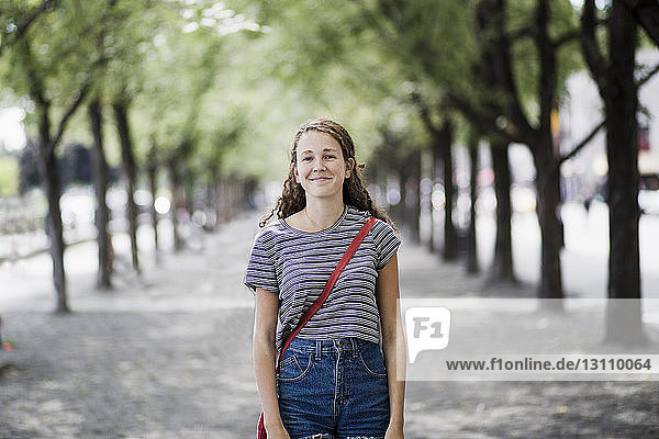 Portrait of smiling woman standing on pathway amidst trees
