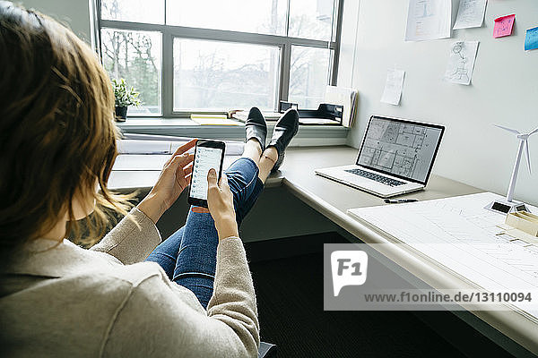Rückansicht einer Geschäftsfrau  die ein Smartphone benutzt  während sie im Büro sitzt