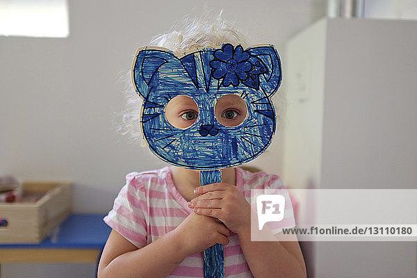 Portrait of girl holding cat mask while standing at home