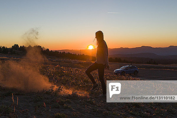 Side view of playful woman standing on field against sky during sunset