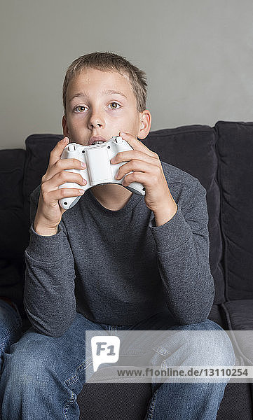 Junge spielt Videospiel  während er zu Hause auf dem Sofa sitzt