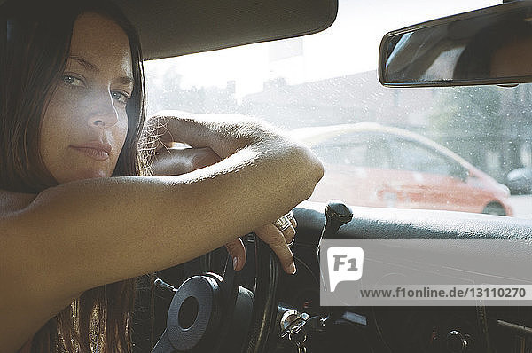 Porträt einer jungen Frau  die sich im Auto auf das Lenkrad stützt