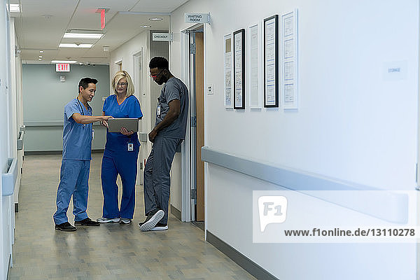 Doctors discussing over laptop computer while standing in hospital corridor